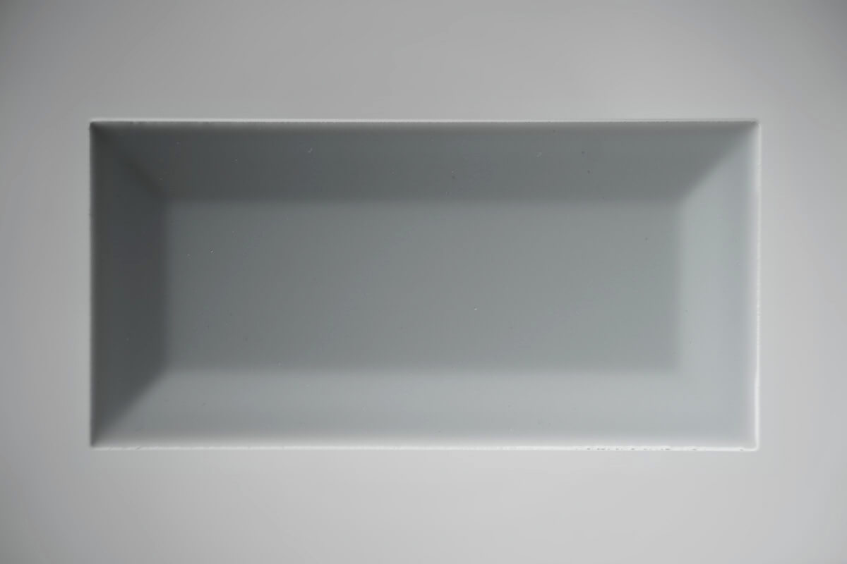 Top-down flat lay of a white beveled ceramic subway tile on a light gray background, tile product photography
