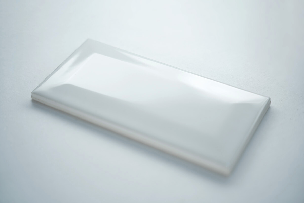 Glossy white beveled subway tile at an angle with smooth highlights along the bevel, ceramic tile product photography
