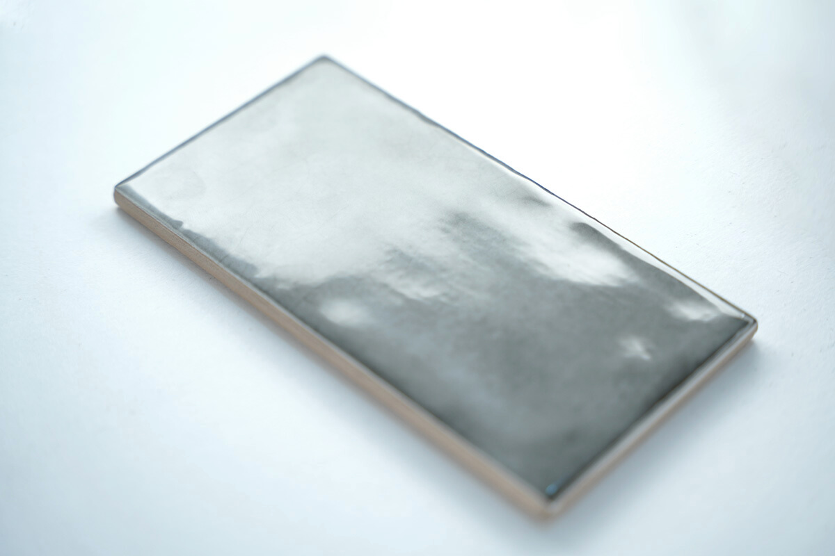 Metallic silver glazed ceramic tile at an angle, showing its handmade surface texture, tile product photography