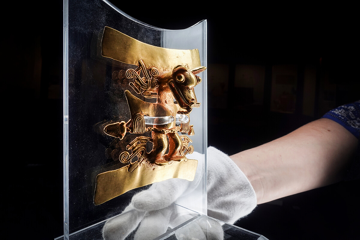 Gold figure mounted on a clear acrylic stand held in a gloved hand, lit with the Halumin H18 lighting device