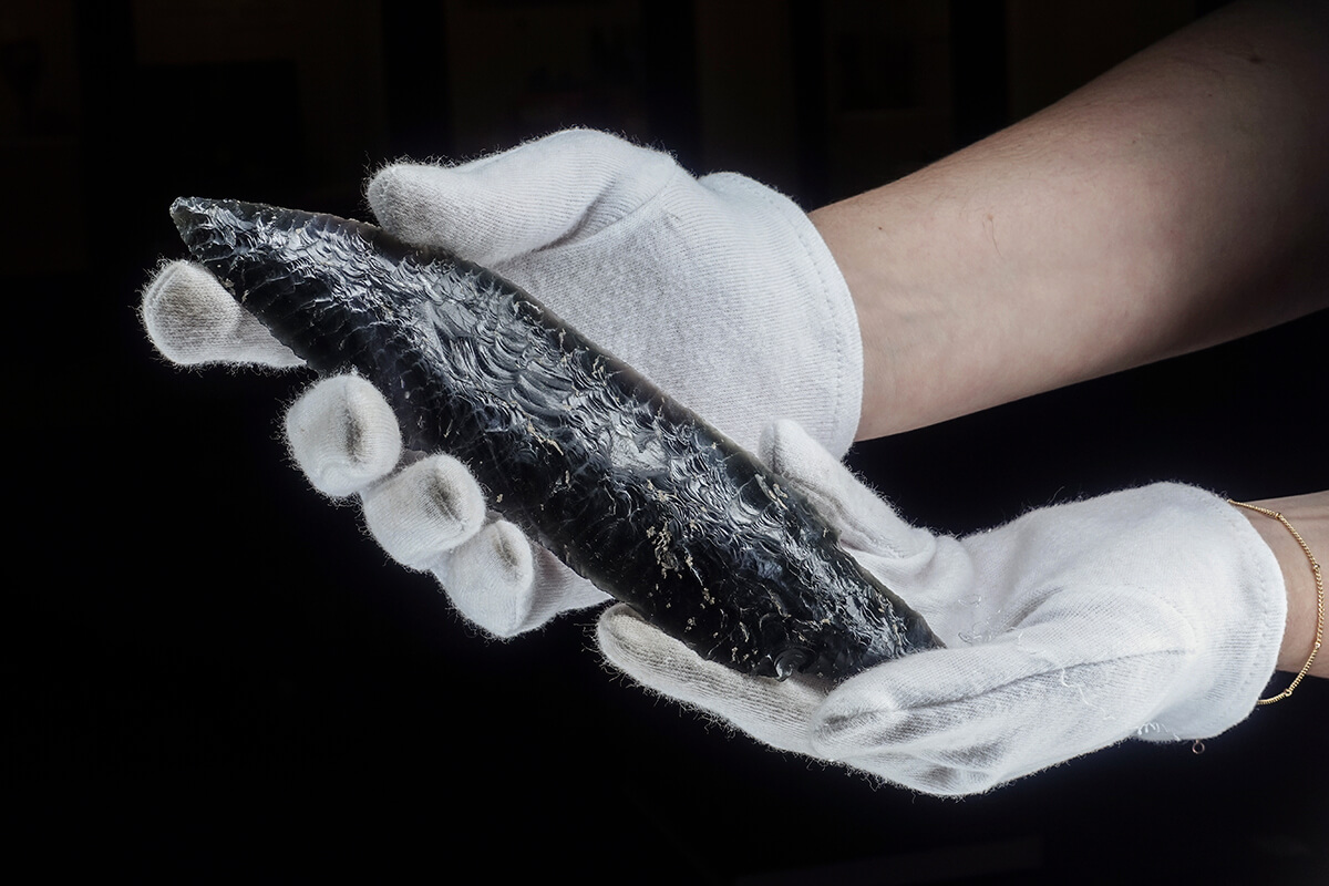 Museum curator holding an obsidian spear point in white cotton gloves, museum artifact photography with the Halumin H18