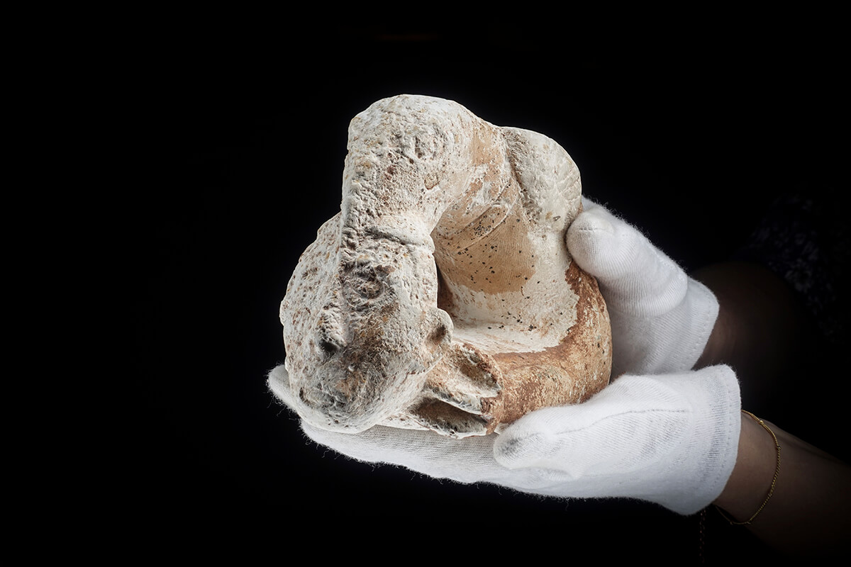 Carved stone pipe at a 3/4 angle held in gloved hands, lit with the Halumin H18 lighting device