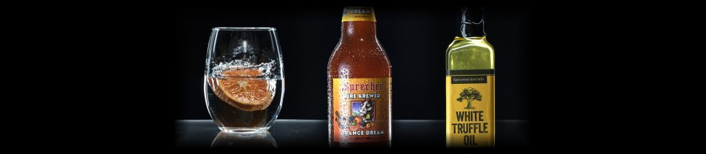 Bottle photography lighting: a glass with an orange slice, a soda bottle and an oil bottle rim-lit on black