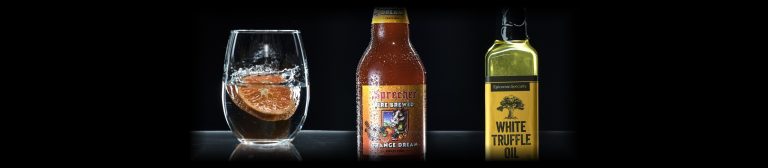 Bottle photography lighting: a glass with an orange slice, a soda bottle and an oil bottle rim-lit on black