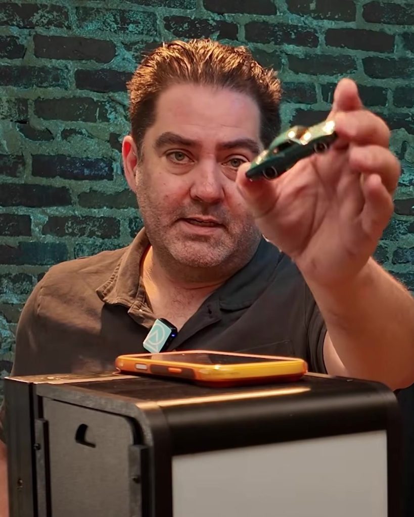 Holding a teal Hot Wheels '68 Plymouth Barracuda Formula S in front of the Halumin-C prototype, with an iPhone lying on top of the light.