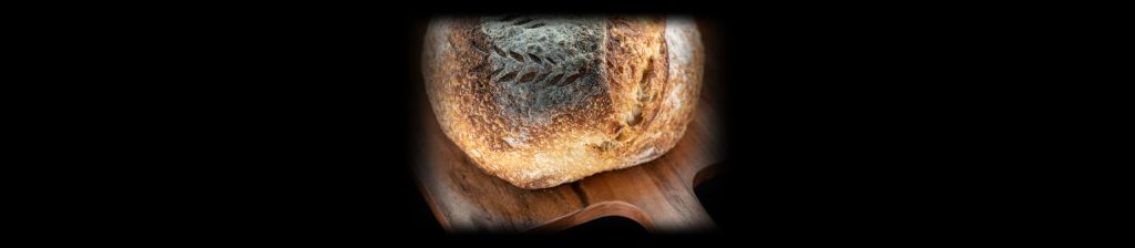 Whole round sourdough loaf on a wooden paddle board, lit with the Halumin H18 lighting device