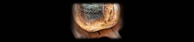 Whole round sourdough loaf on a wooden paddle board, lit with the Halumin H18 lighting device