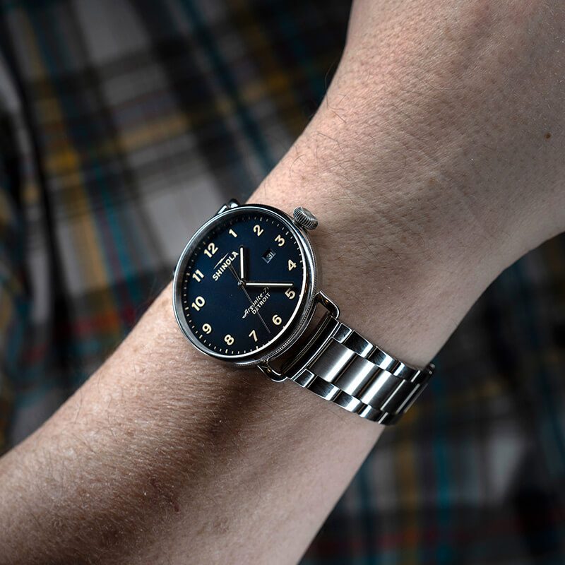 Shinola watch with a navy dial and steel bracelet on the wrist, lit with the Halumin H18